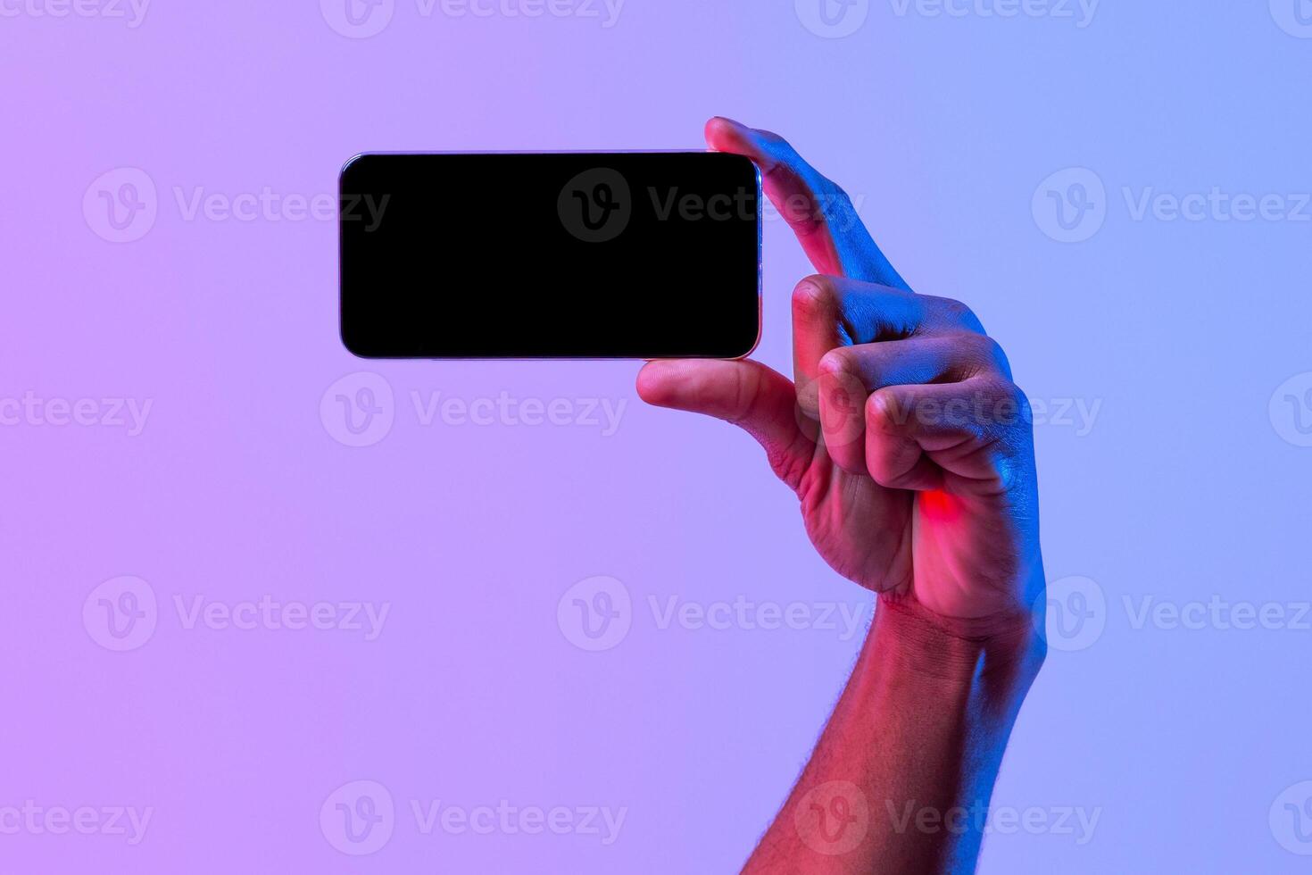 Black Male Hand Holding Blank Smartphone In Horizontal Orientation Over Purple Neon Background, African American Man Demonstrating Copy Space For App Or Mobile Game Design, Mockup Image photo