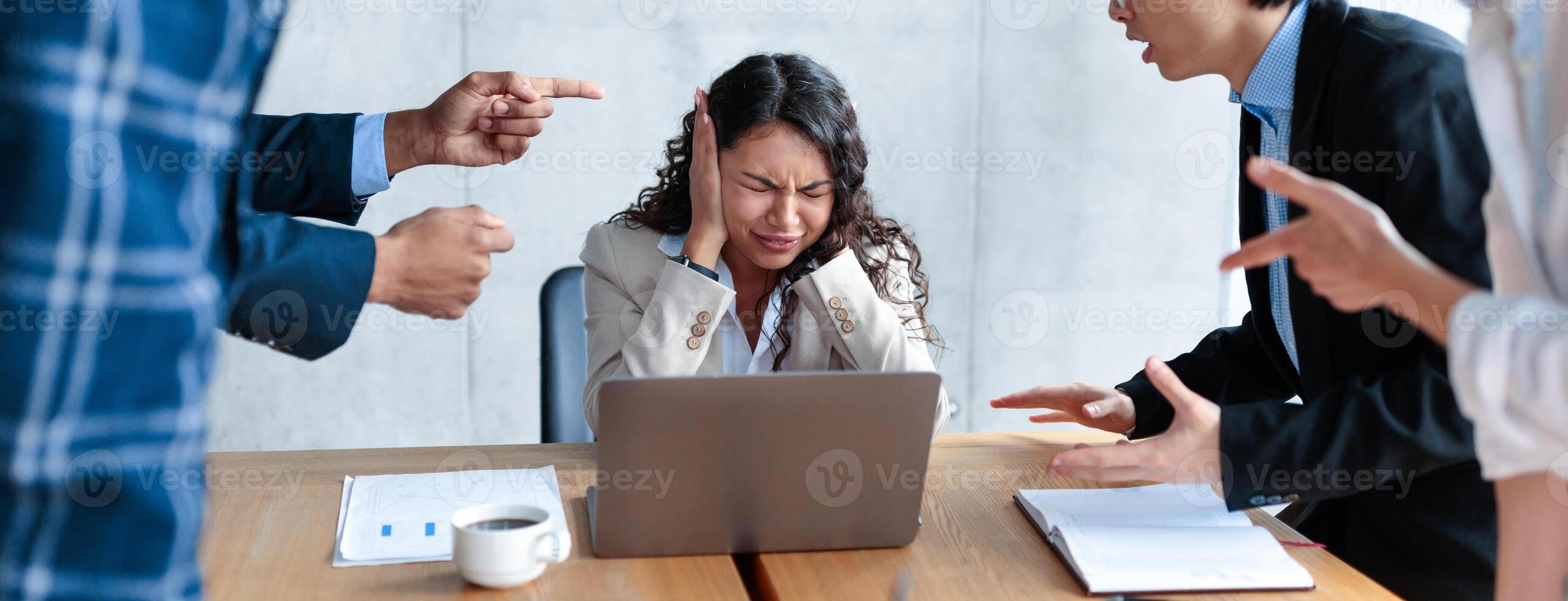 Conflict At Work. Unhappy Victimized Businesswoman Covering Ears Not Listening To Aggressive Colleagues Shouting At Her Sitting At Desk In Modern Office. Adult Bullying, Blaming, Communication Problem photo