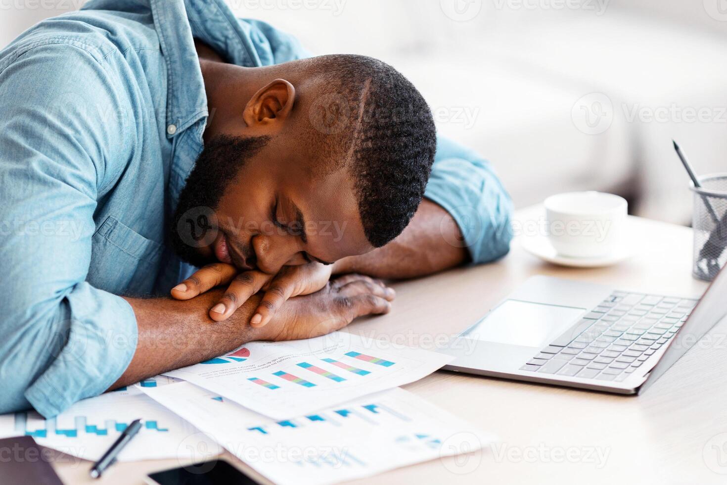 Sleep At Work. Exhausted black male freelancer napping at desk at home office, overworked african american man placed head on hands, tired after working with papers and laptop, closeup shot photo