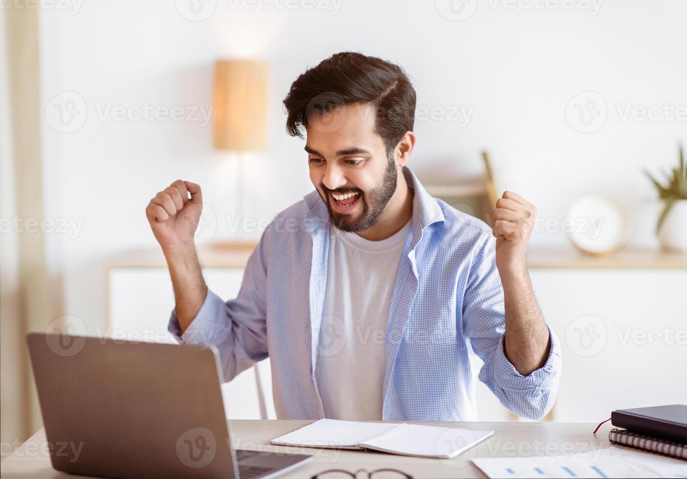 Promotion News. Overjoyed Arab Man Looking At Laptop Screen And Celebrating Success, Excited Man Sitting At Desk With Computer, Raising Fists And Exclaiming With Joy, Emotionally Reacting To Email photo