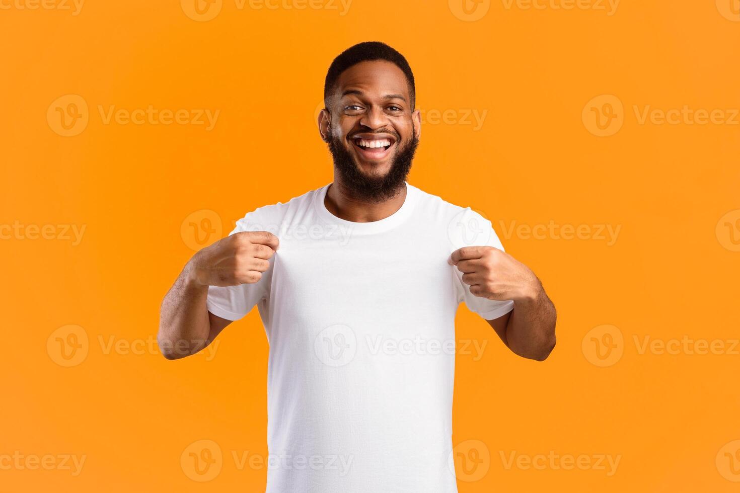 Cheerful Black Man Showing His White T-Shirt Smiling To Camera Standing Over Yellow Studio Background. Look There, Check This Out Concept. T-Shirt Mockup, Template For Your Text. Panorama photo