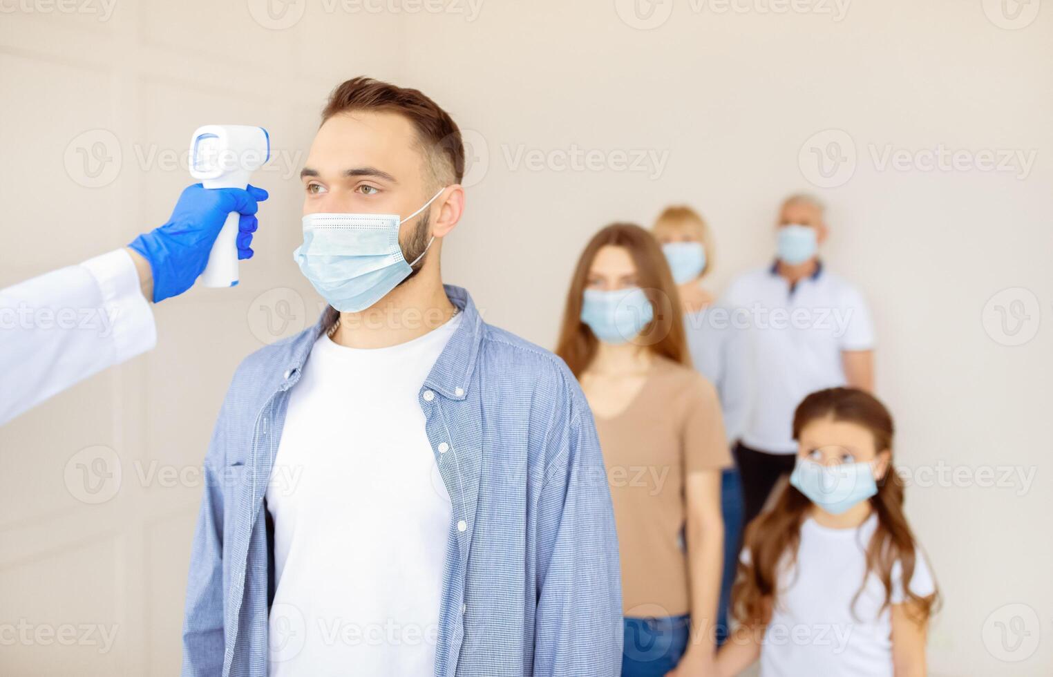 Doctor checking patient's temperature with digital thermometer at clinic waiting room, blank space. People waiting in queue for coronavirus vaccination. Covid-19 population immunization concept photo