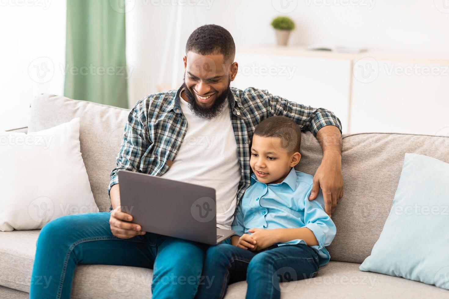Black Daddy And His Kid Son Watching Movie On Laptop Online Sitting Hugging On Sofa, Spending Weekend Together At Home. Technology And Gadgets, Family Of Two Using Computer In Living Room Indoors photo