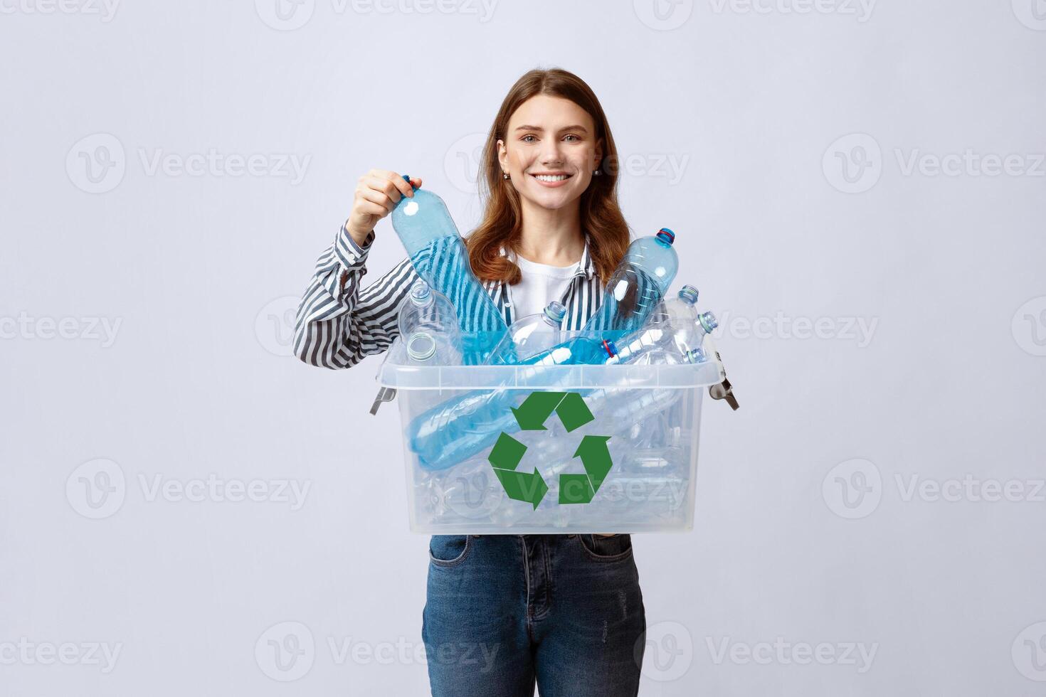 Waste For Recycling. Cheerful Young Woman Carrying Container Box With Empty Plastic Bottles, Positive Millennial Lady Sorting Garbage, Enjoying Zero Waste Living, Standing On Grey Studio Background photo