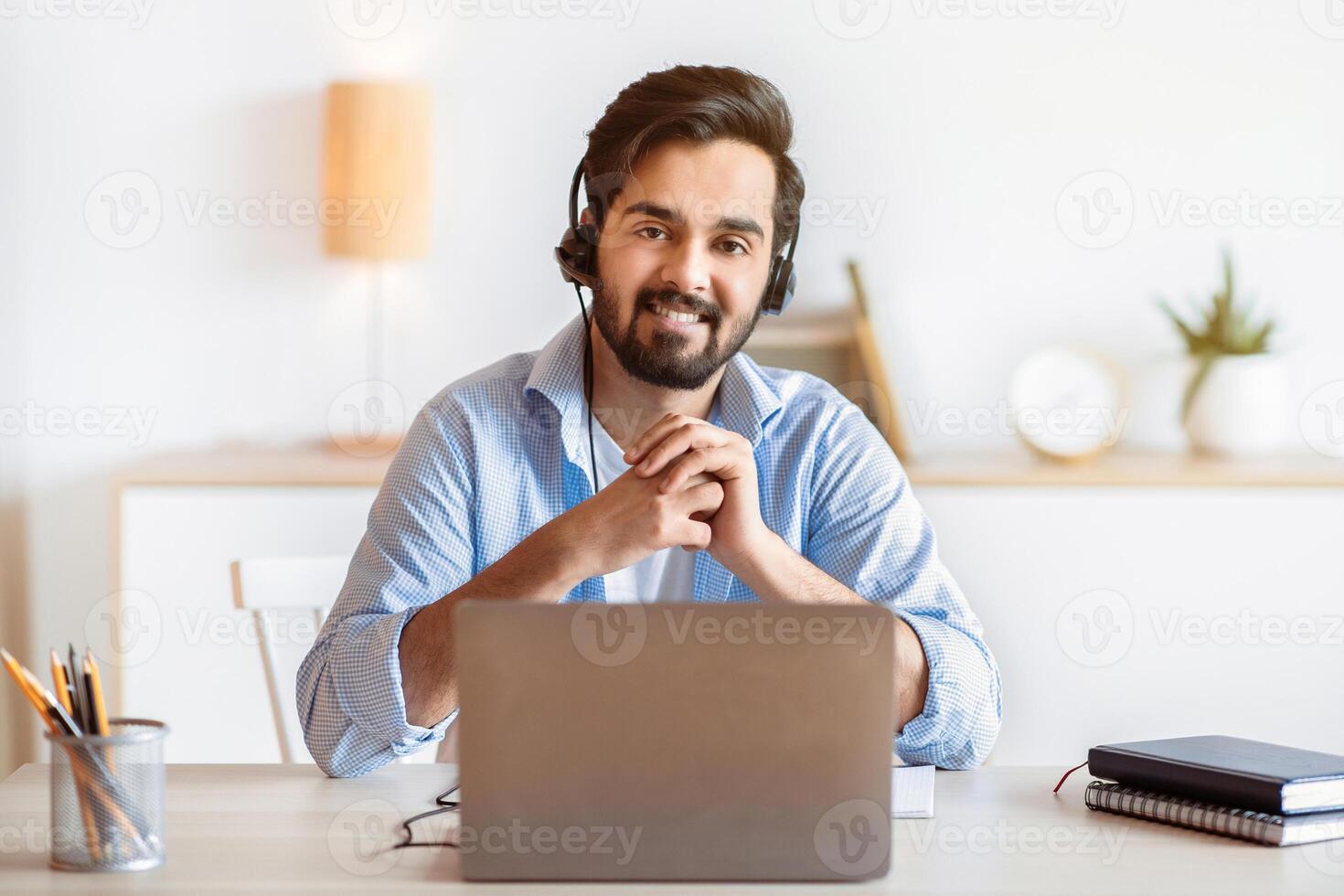 Remote Job Opportunities. Portrait Of Smiling Arab Man Hotline Manager In Headset Posing At Workplace, Eastern Guy Sitting At Desk With Laptop At Home Office And Looking At Camera, Copy Space photo