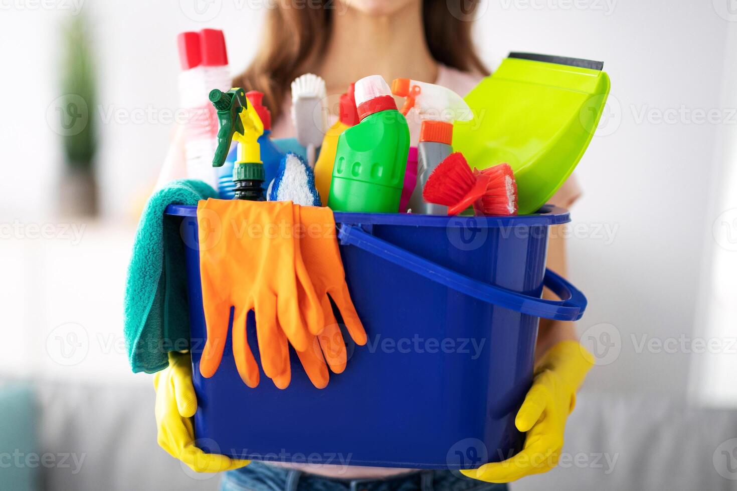Unrecognizable millennial maid holding bucket with cleaning supplies indoors, closeup of hands. Cropped view of housewife with detergents, ready for house cleanup. Sanitary service concept photo