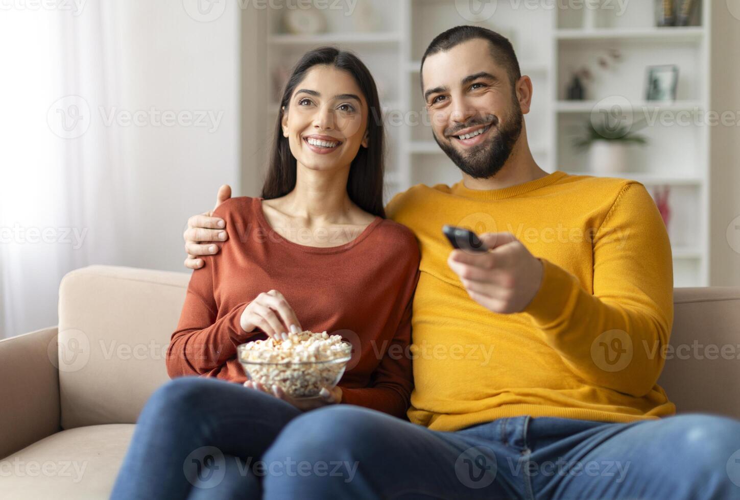 Home Relax. Happy Young Married Couple Watching Tv In Living Room, Smiling Millennial Spouses Eating Popcorn Together While Relaxing On Comfortable Couch, Man Holding Remote Controller, Closeup Shot photo