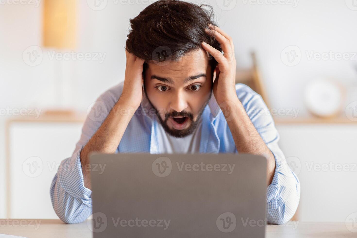 Deadline Stress. Frustrated arab man looking at laptop screen and touching head in shock, eatern freelancer guy suffering business problems while working online on computer at home office, closeup photo