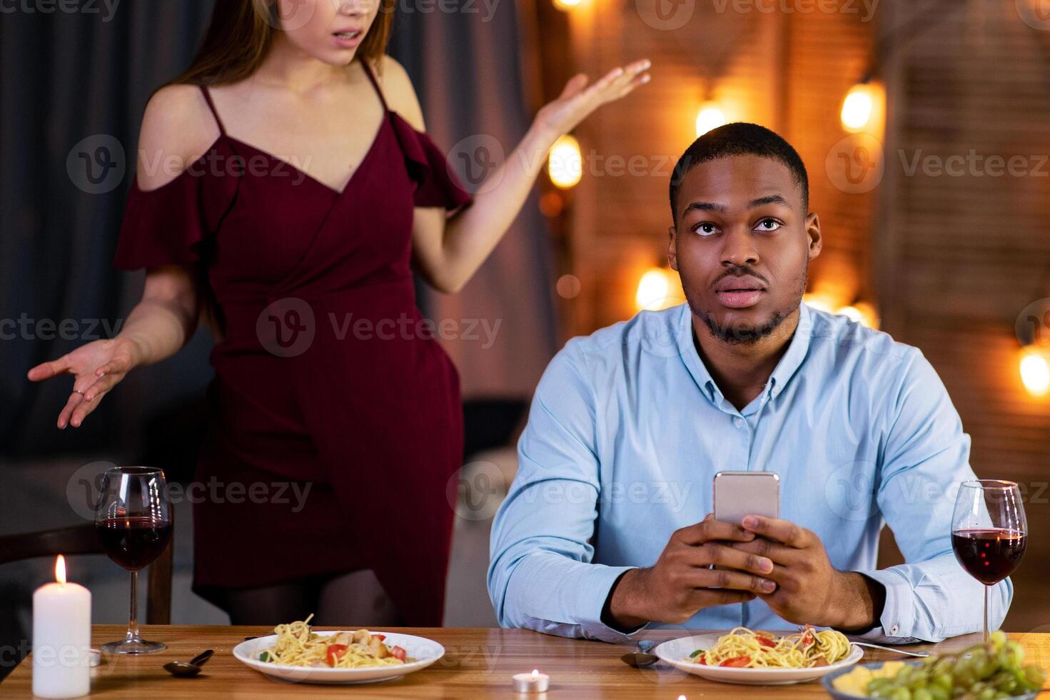Annoyed young woman angry to her black boyfriend stuck in smartphone during romantic date in cafe, interracial couple having conflict while dining in restaurant on Valentine's day, free space photo