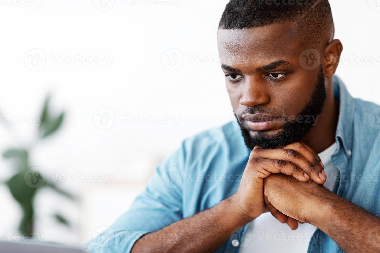 Deep in thoughts. Portrait of pensive millennial African American man leaning head on hands, black young guy thinking about solution with serious face expression, closeup shot with copy space photo