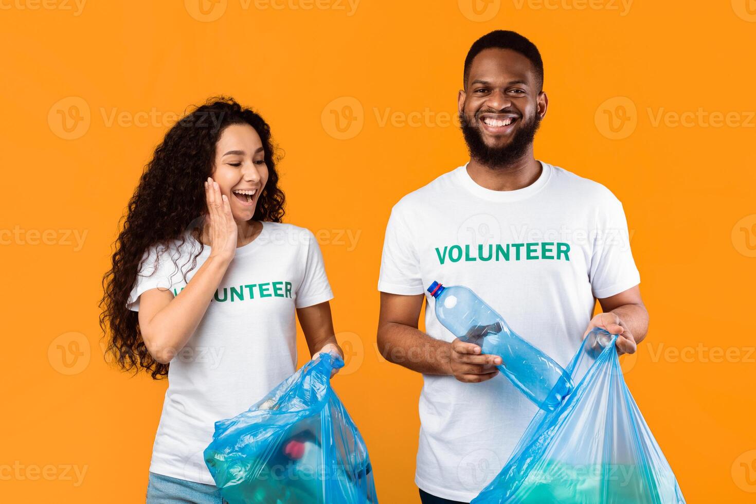 Excited Multicultural Female And Male Volunteers Picking Plastic Bottle In Garbage Bag Cleaning Environment And Picking Littter Standing Over Yellow Background, Studio Shot photo