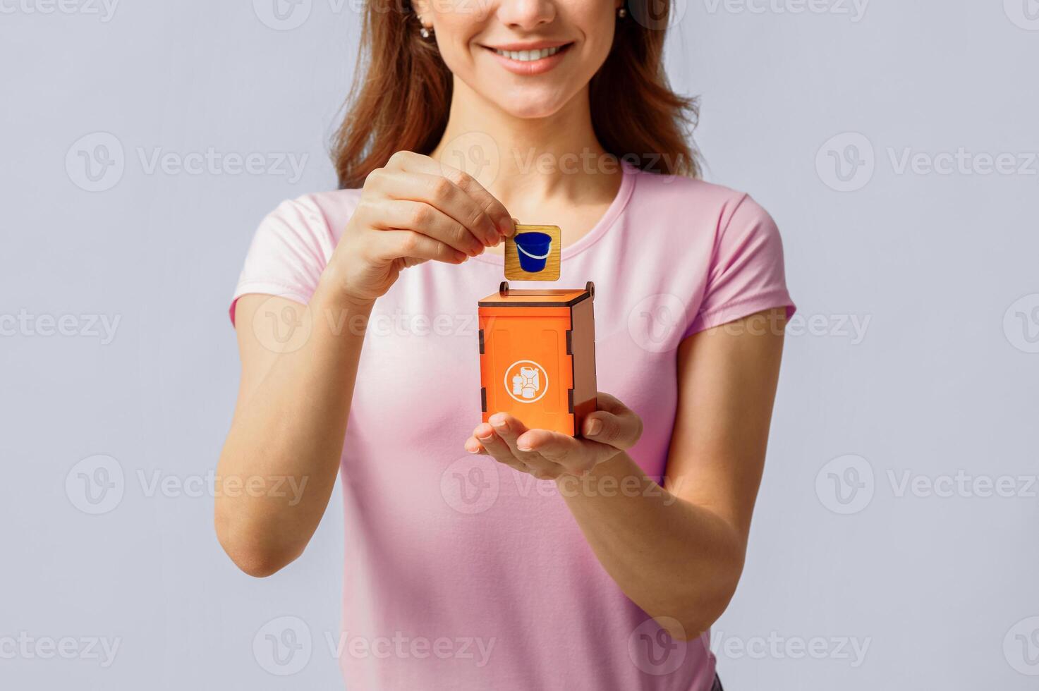 A woman smiles as she drops a recyclable item into a small orange recycling bin. Her commitment to eco-friendly practices reflects her dedication to sustainability and environmental awareness. photo