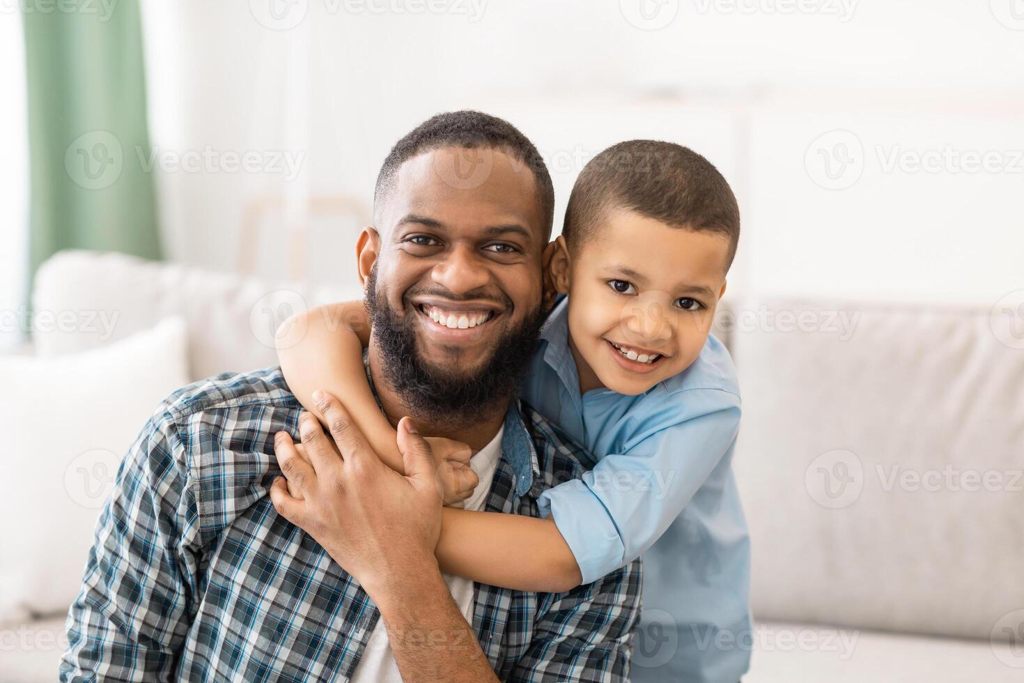 Portrait Of Cheerful African Father And Son Hugging Posing Smiling To Camera Sitting On Couch At Home. Happy Fatherhood And Childhood, Family Happiness Concept photo