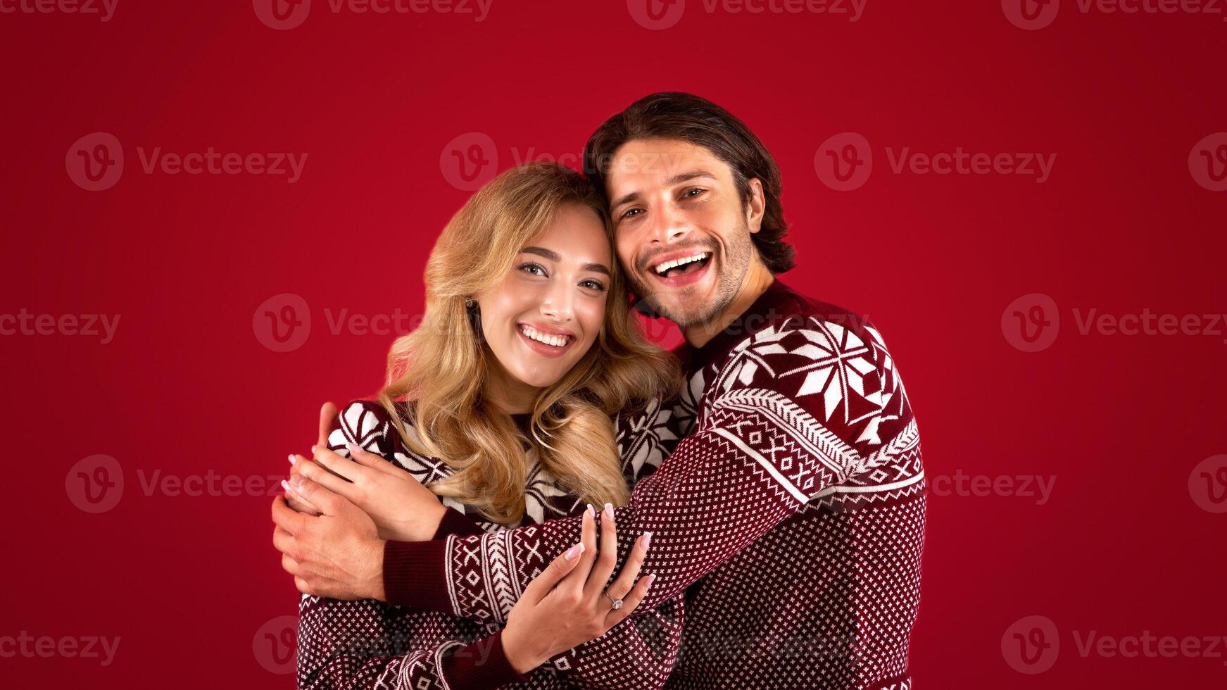 It's Christmas. Affectionate young couple in winter clothes hugging on red background photo