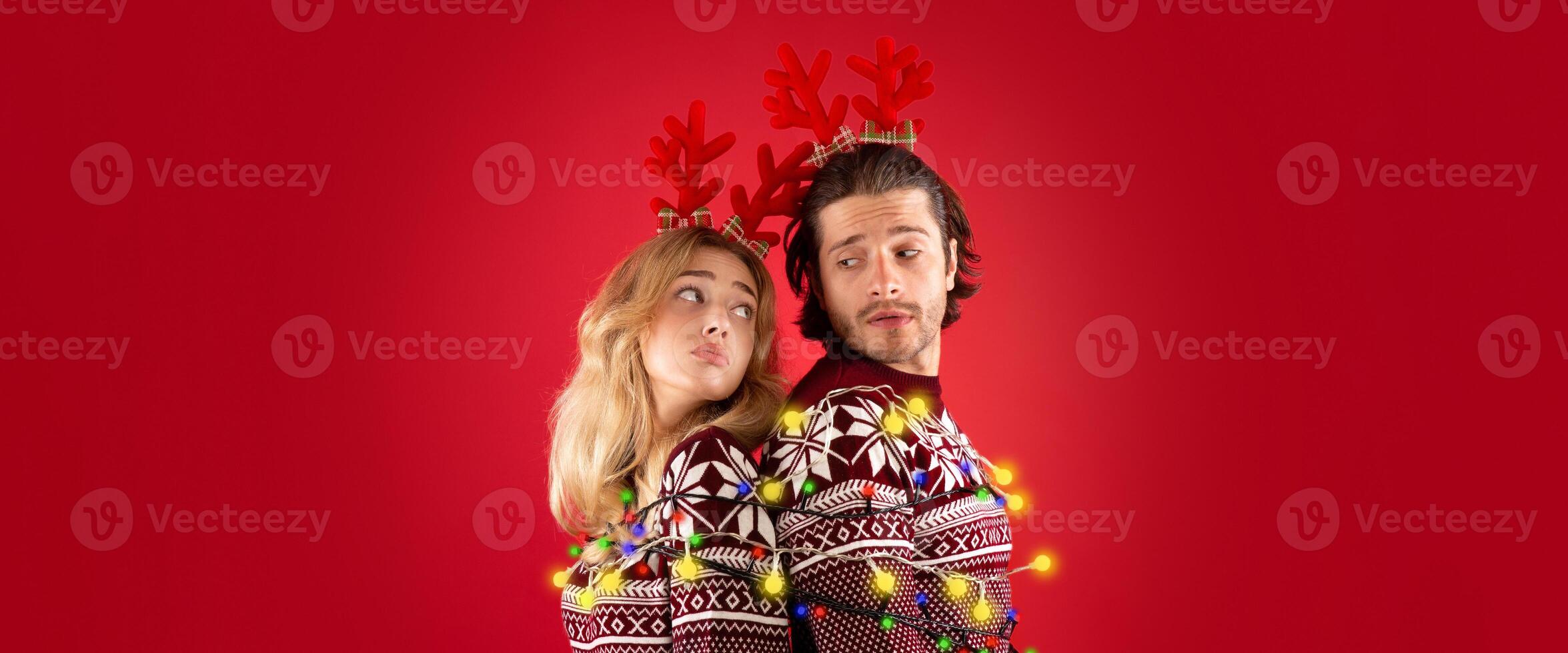 Young man and his girlfriend tied together with Christmas lights over red background photo