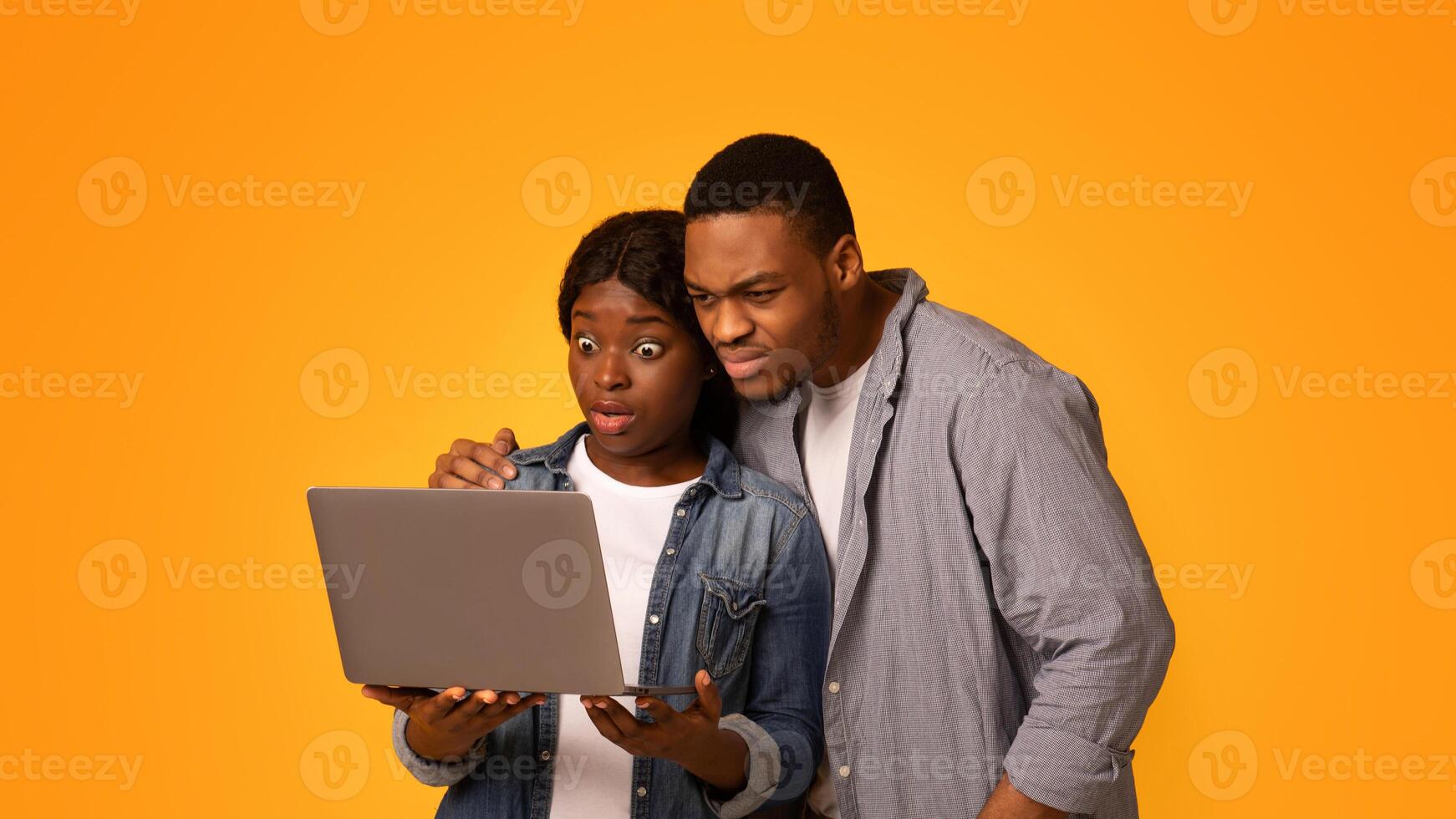 Shock Content. Overwhelmed African American Couple Looking At Laptop Screen, Young Black Man And Woman Holding Computer, Suffering From Internet Scam While Standing On Yellow Background, Free Space photo