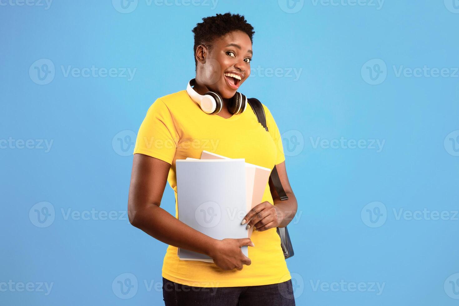 African American Oversized Female Student Holding Books Posing Smiling To Camera Standing Over Blue Background In Studio. University And College Study, Knowledge Concept photo