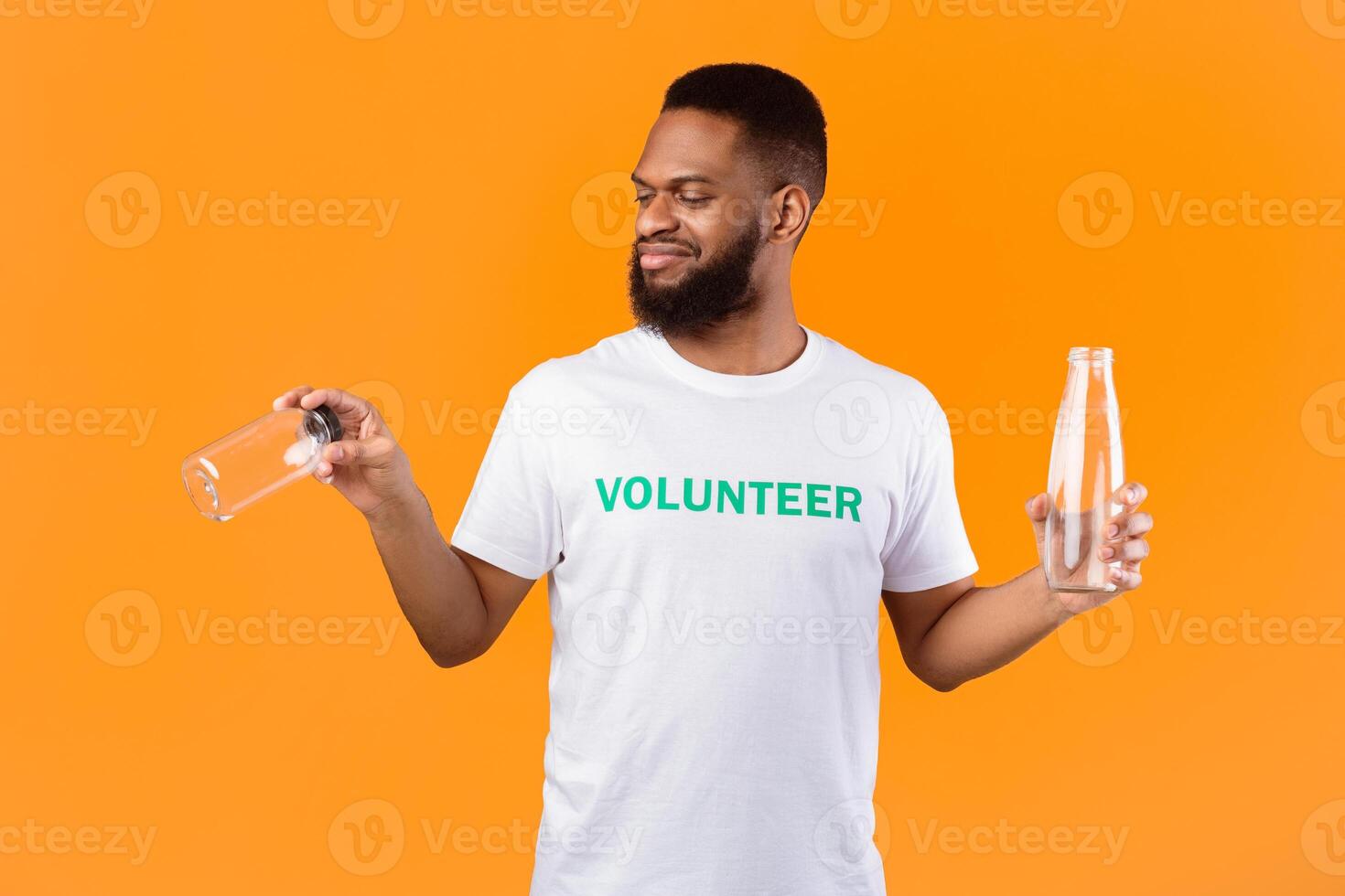 No More Plastic. African Volunteer Guy Choosing Between Glass And Plastic Bottle Standing Over Yellow Studio Background. Ecology And Environment Concept photo