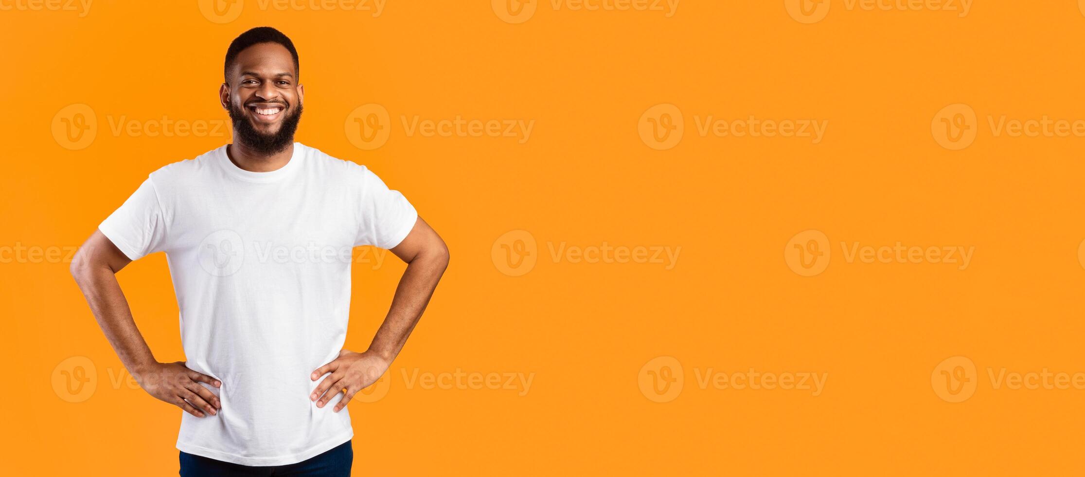 Happy African American Man Standing With His Hands On Hips Posing Near Empty Space For Text On Yellow Studio Background, Smiling To Camera. Advertisement Banner Concept. Panorama photo