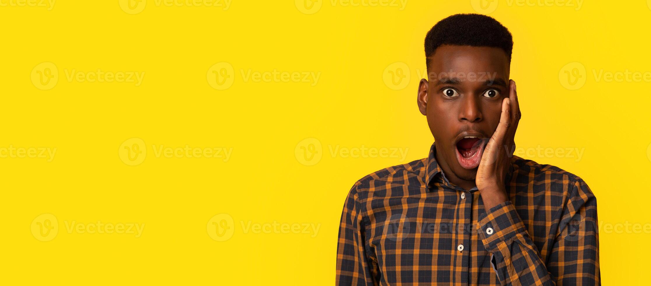 Unbelievable. Portraif Of Shocked Young Black Man Touching Face With Excitement, Amazed African American Guy Standing With Opened Mouth And Looking At Camera, Isolated On Yellow Background, Copy Space photo