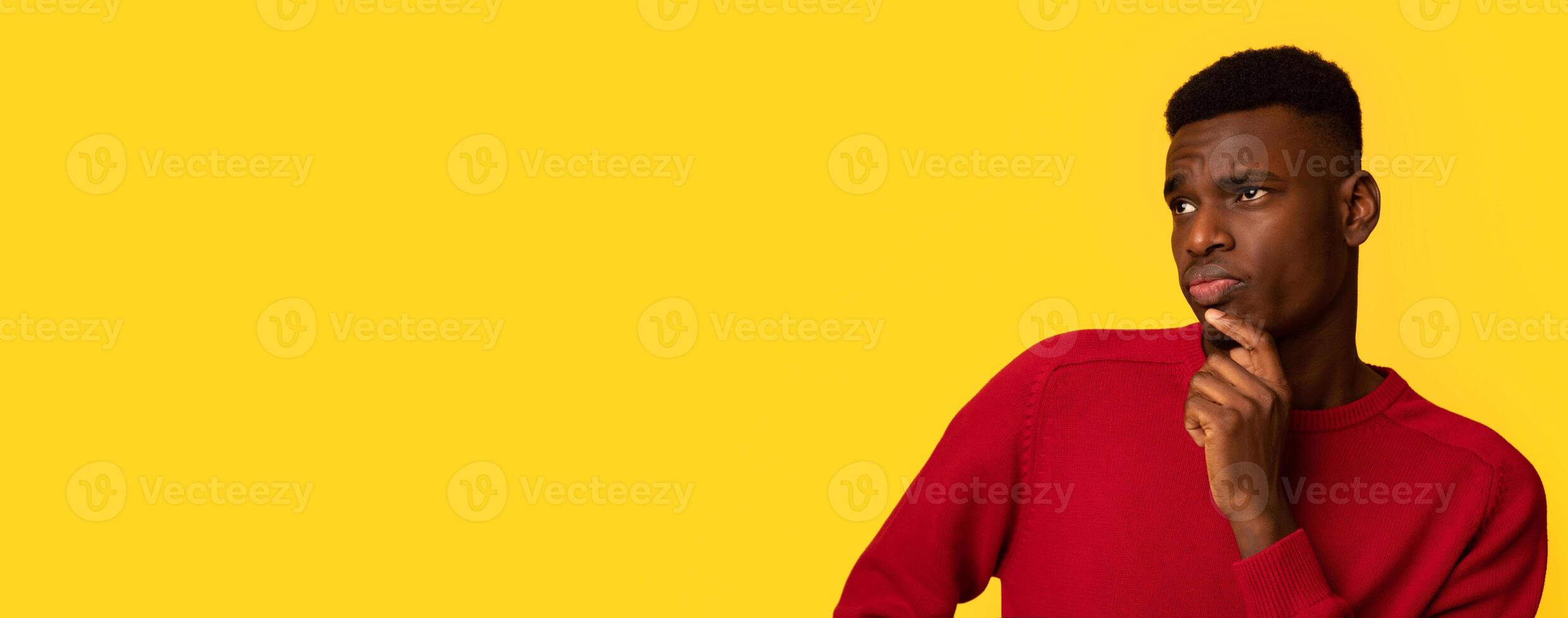 Doubtful Young Black Man Looking Aside At Copy Space With Curiousity. Unsure African Guy Touching Chin, Thinking About Interesting Offer While Standing Isolated Over Yellow Background, Panorama photo