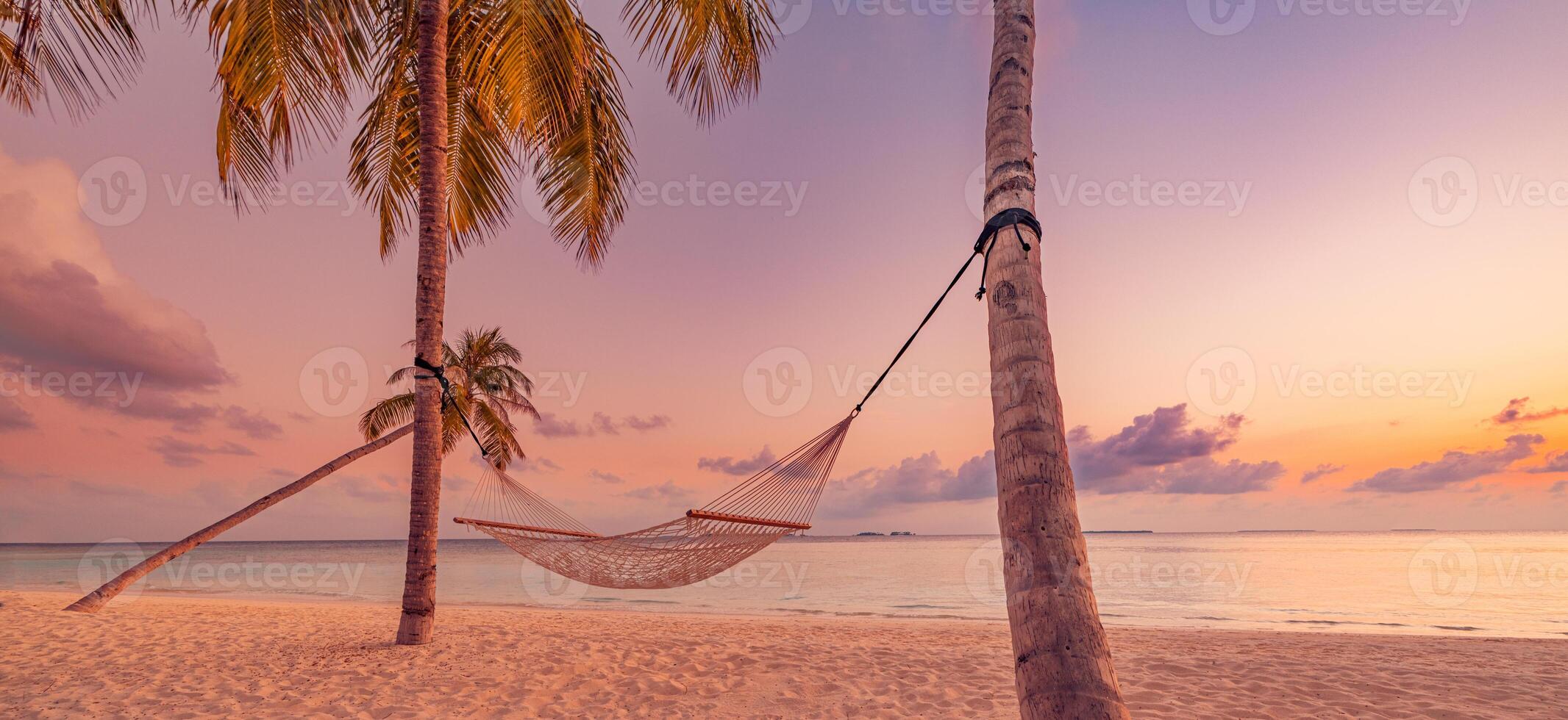 Panoramic sunset scene with swing and hammock under palm trees by the sea, dreamy seascape and inspiring sky with clouds creating a stunning summer vacation travel background on a tropical island photo