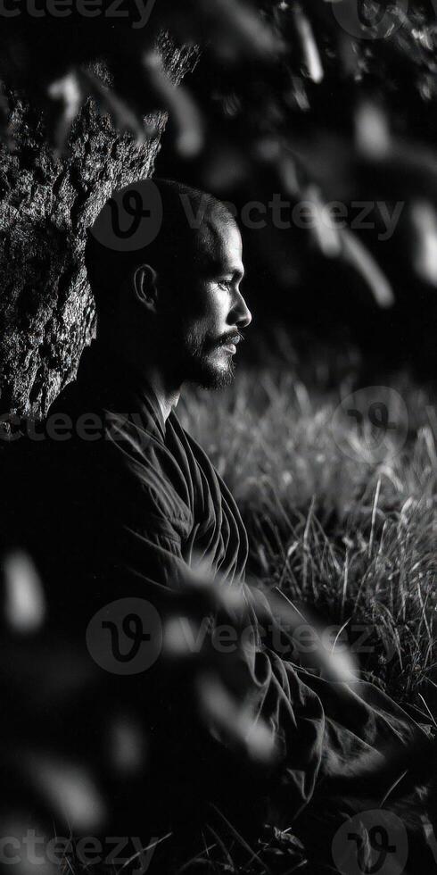 Monk rests against tree in nature, looking contemplative photo