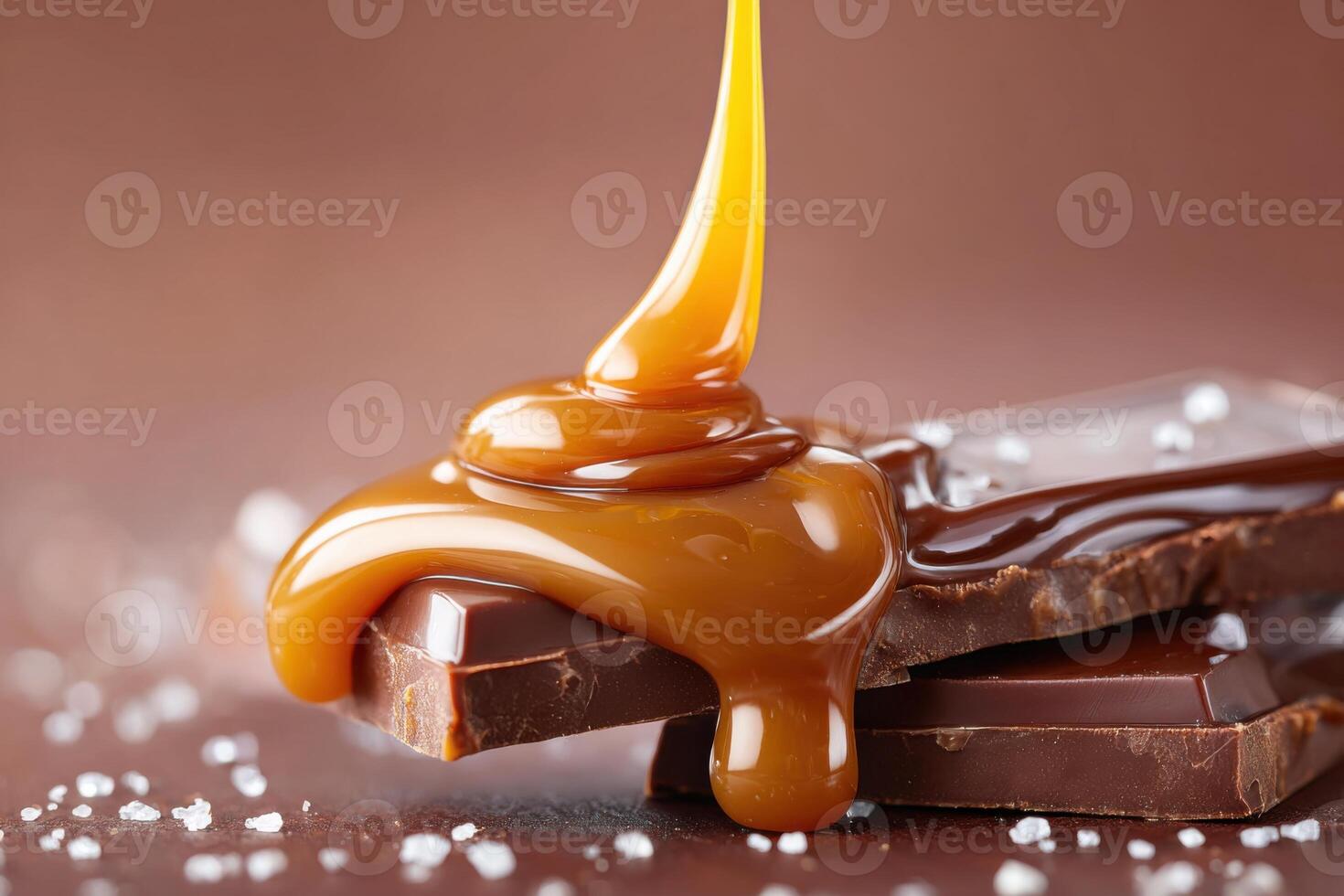 Liquid caramel pouring over pieces of dark chocolate with salt grains photo