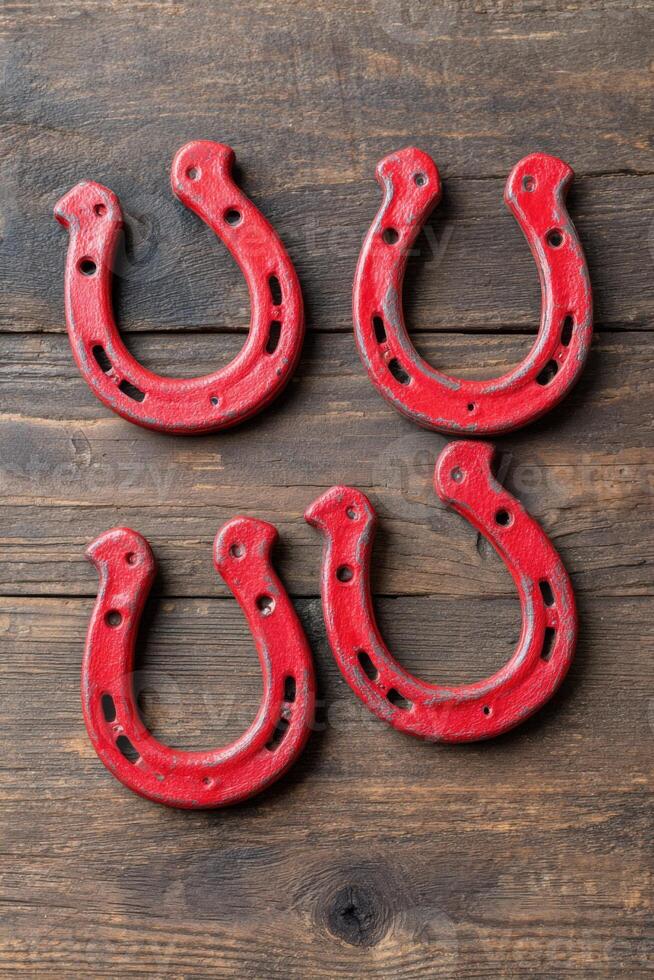 Four red horseshoes arranged on a rustic wooden surface, showcasing their unique shapes and textures, symbolizing good luck and tradition in equestrian culture photo