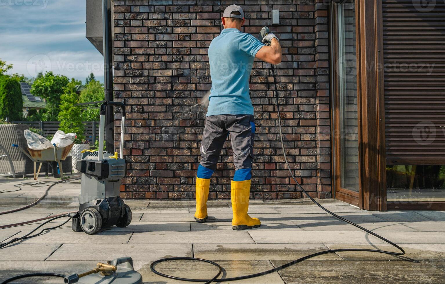 Person Cleaning Exterior Wall With Pressure Washer on a Sunny Day in a Residential Area photo