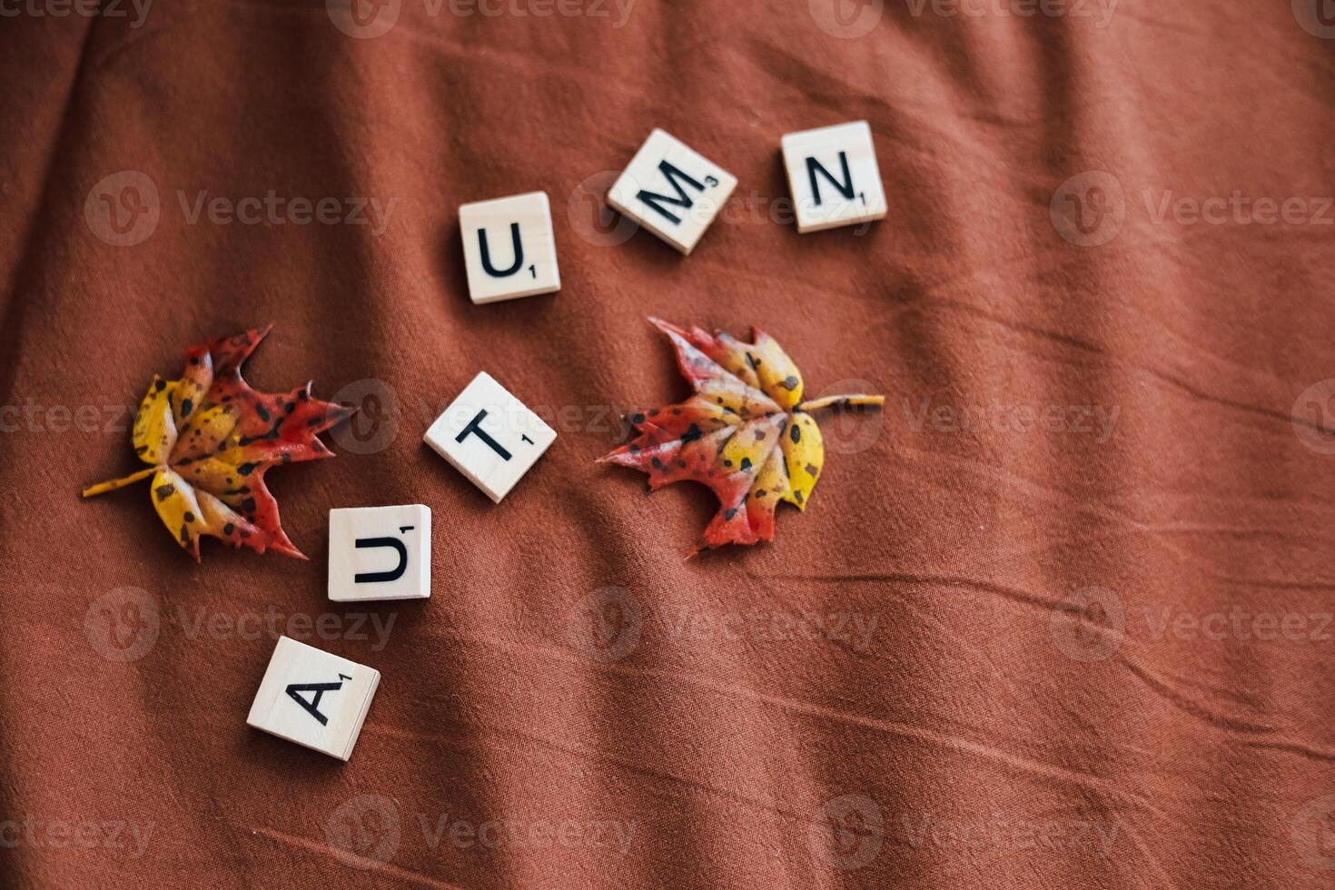 Colorful autumn leaves arranged with wooden letters spelling autumn on brown fabric photo