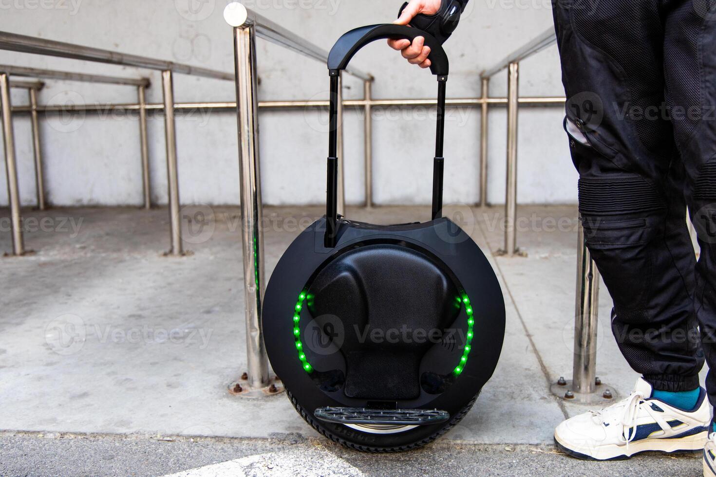Modern electric unicycle being carried by a person in urban environment near railings photo