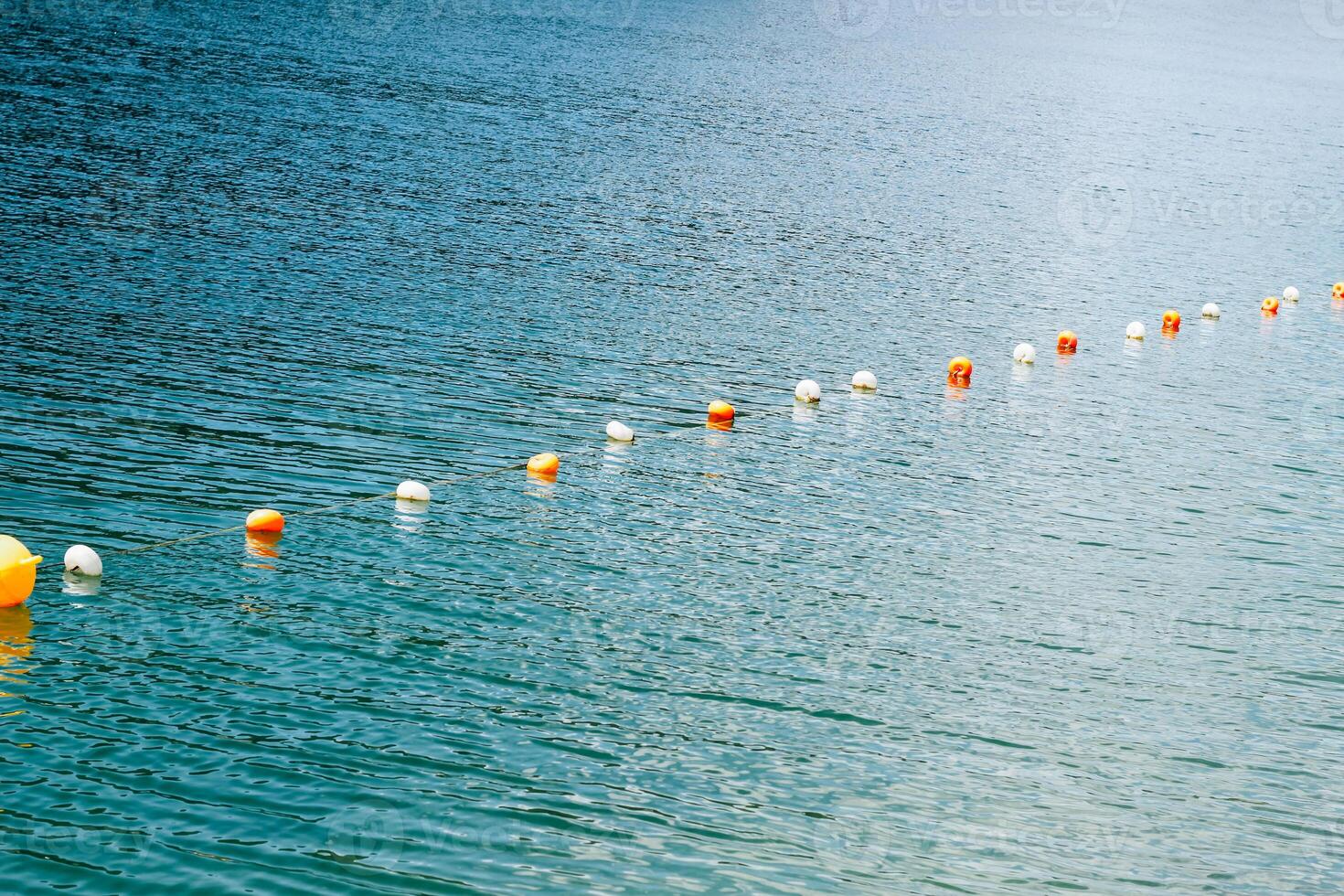 Bright buoy markers floating along a tranquil lake during a sunny day photo