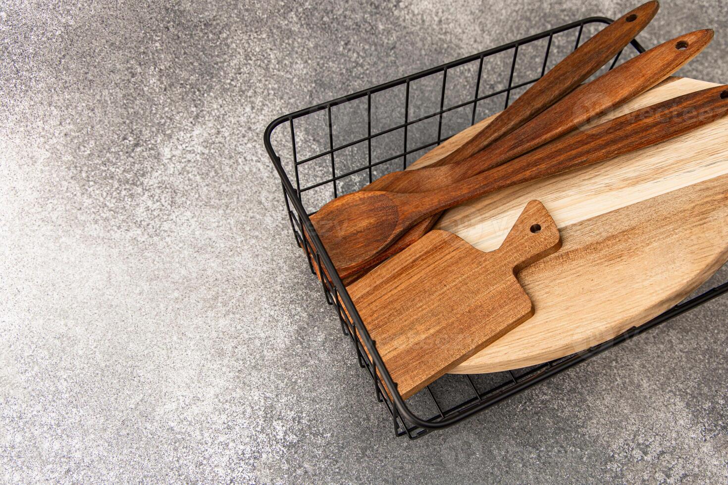 Wooden cooking utensils and cutting board arranged neatly in a wire basket on a kitchen counter photo