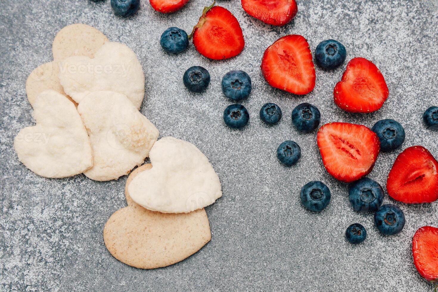 en forma de corazon galletas y Fresco fresas con arándanos en un gris superficie foto