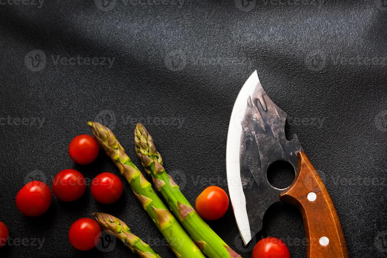 Fresh vegetables and a unique knife are displayed on a dark background for meal preparation photo