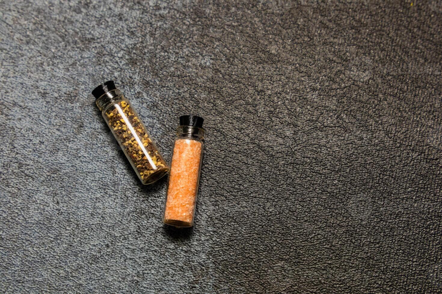 Two small spice jars on a dark textured surface showcasing colorful seasonings photo
