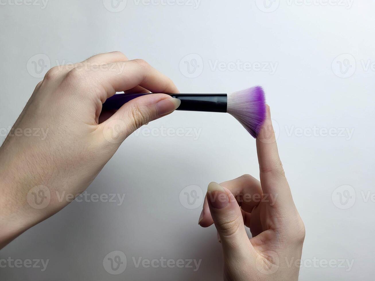 The hands hold a black cosmetic brush with lilac bristles photo