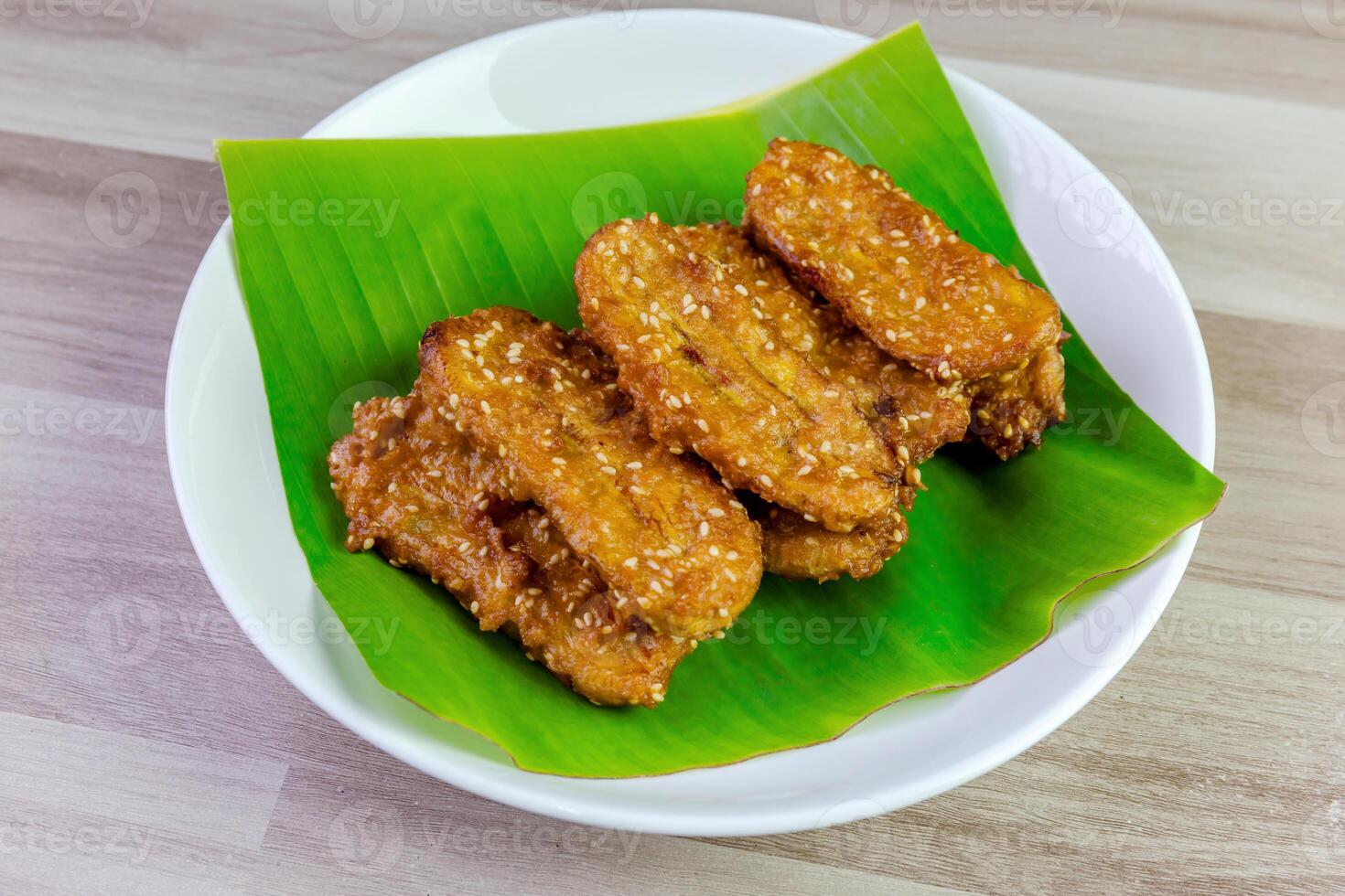 Crispy Thai fried bananas with sesame seeds served on a banana leaf in a white plate, Fried bananas is a traditional Asian snack with sweet, crunchy texture. Top view shot photo