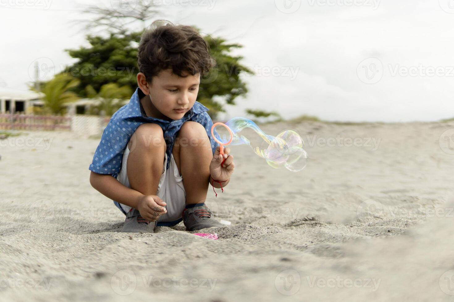 Hispanic little child making soap bubbles on the beach on a cloudy day photo