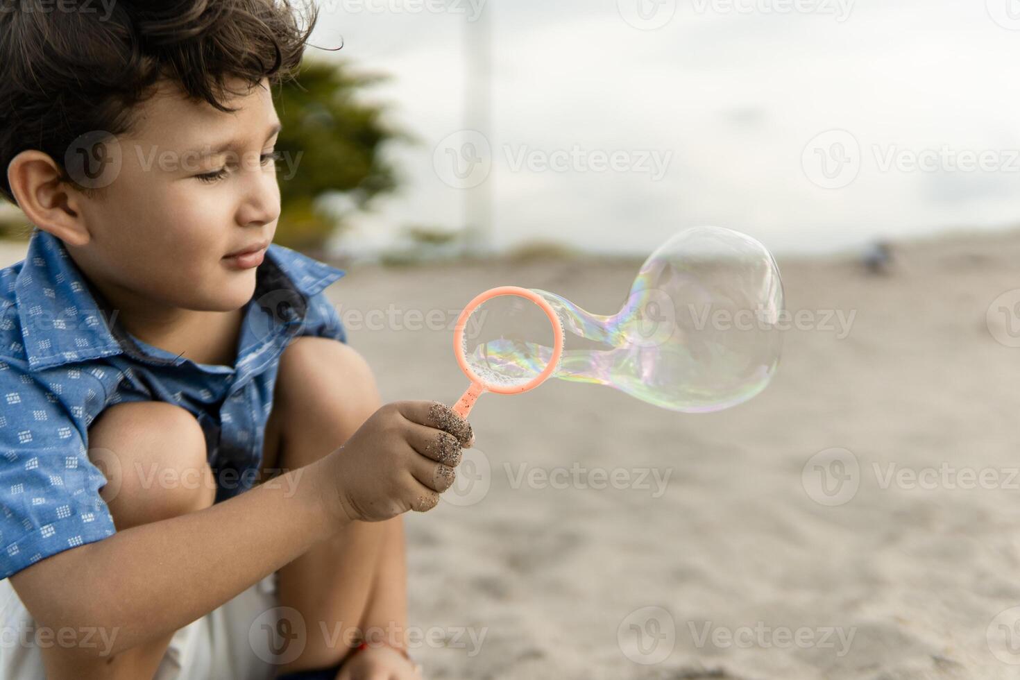 Little boy making soap bubbles on the beach with a bubble blower toy photo