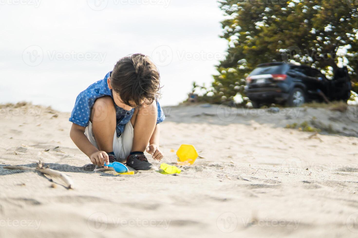 Child having fun with beach toys near family car and tree photo