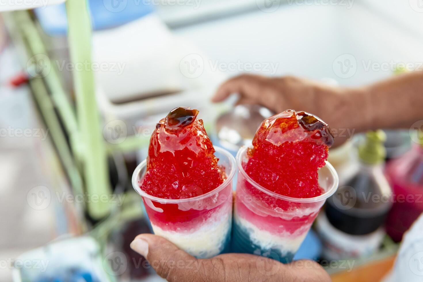 Street vendor holding two cups of colorful shaved ice with syrup topping photo