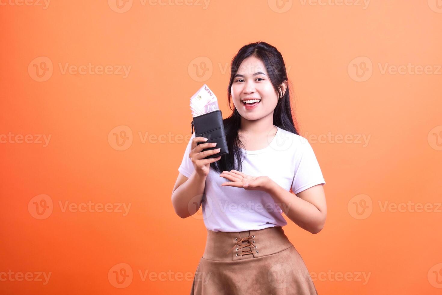 A Smiling Woman Holds a Wallet Full of Money Against an Orange Background photo