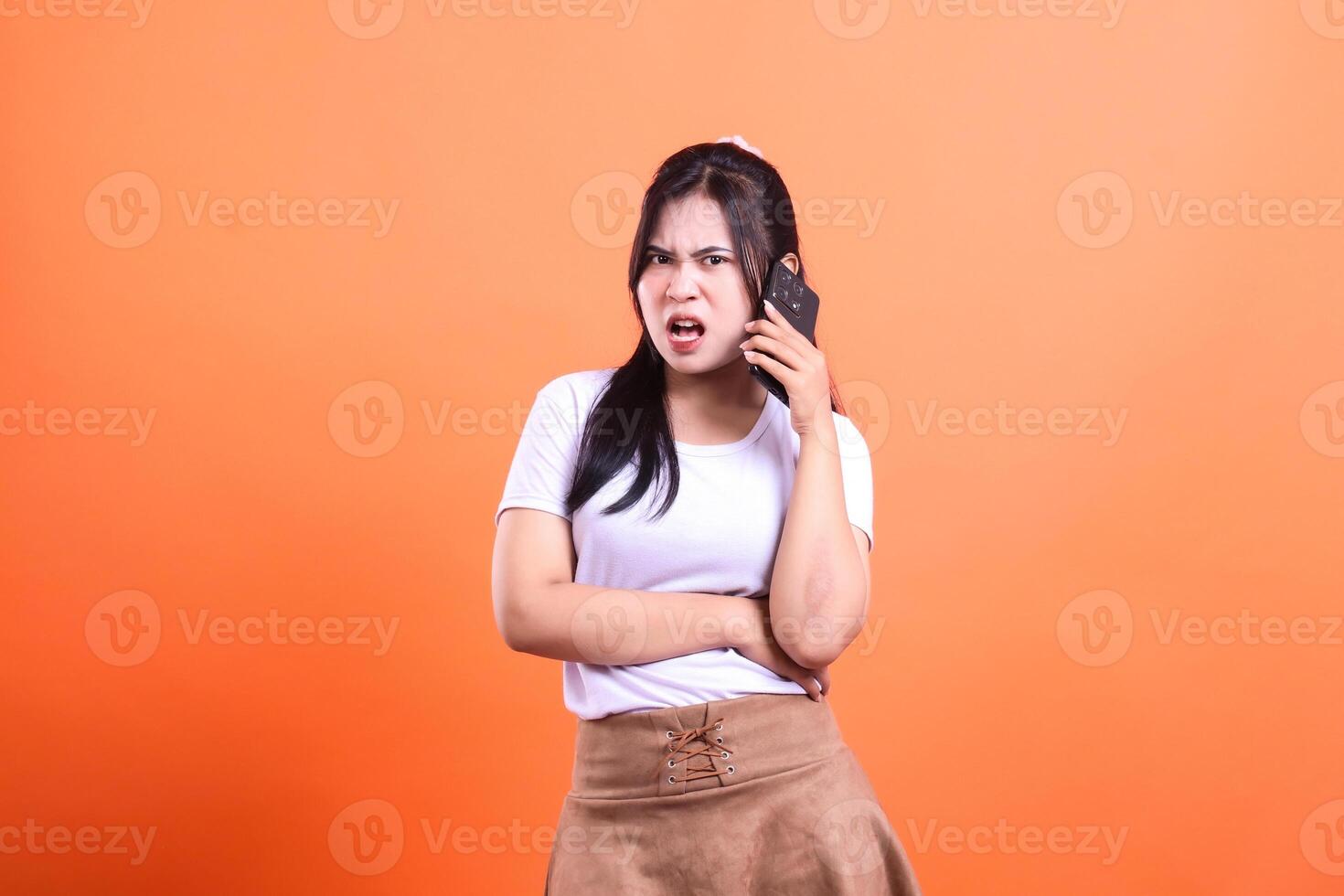 Woman with phone on bright orange background showing displeased expression photo