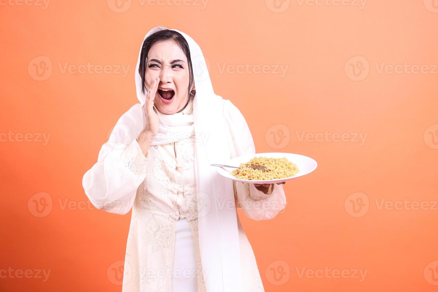 A muslim woman is yelling while carrying a plate of pasta and using a hijab. isolated on a orange background. photo