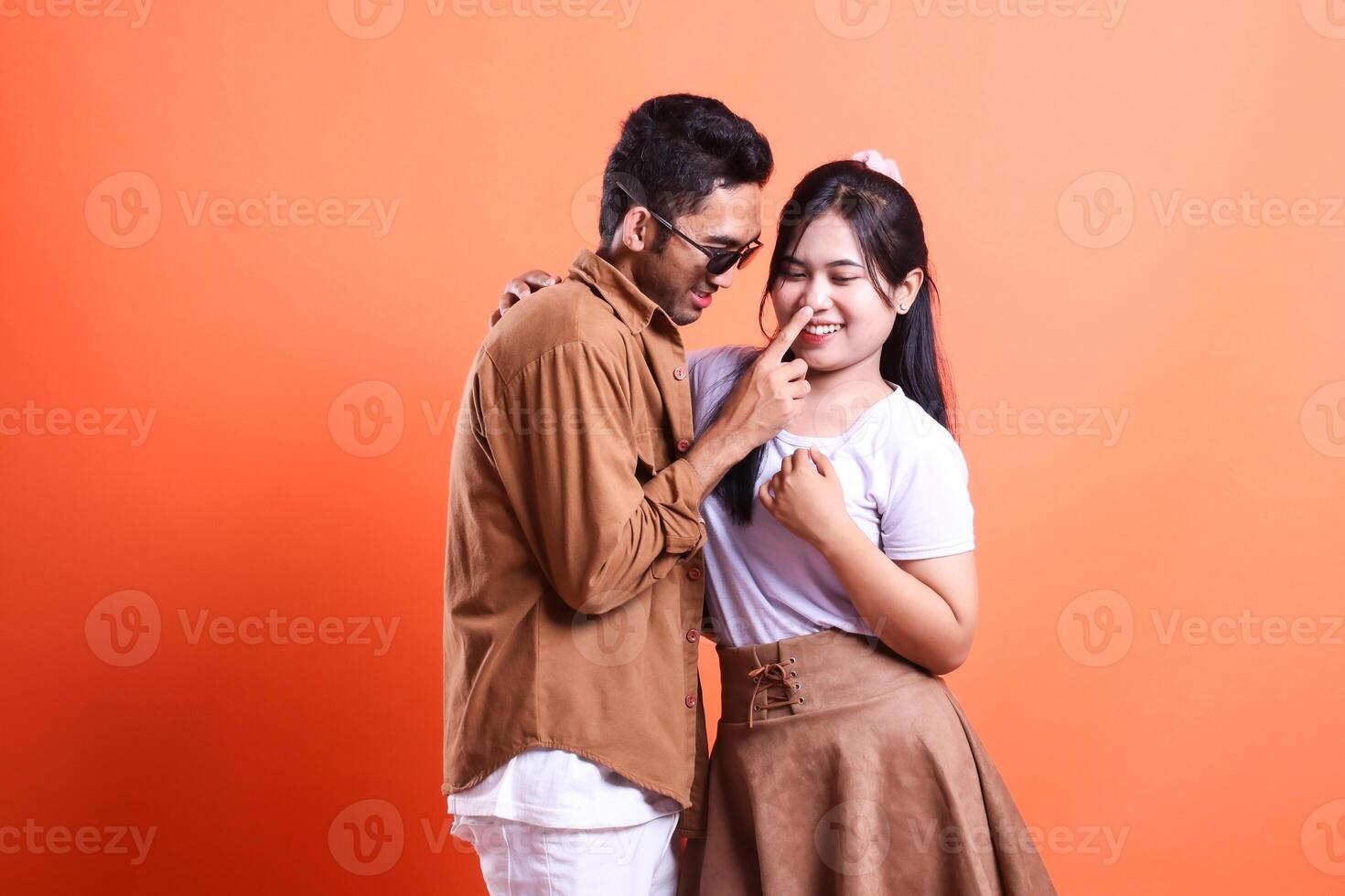 A man playfully touches a woman's nose in a studio shot with orange background photo