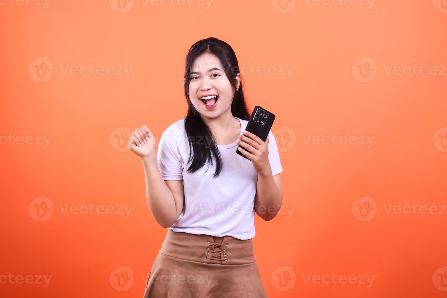 Excited woman holding phone with orange background, isolated image for content photo