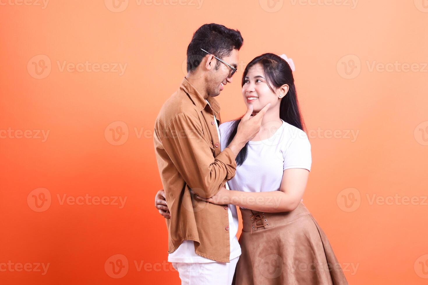 A loving couple embracing each other with orange background in the studio, looking into each other eyes photo