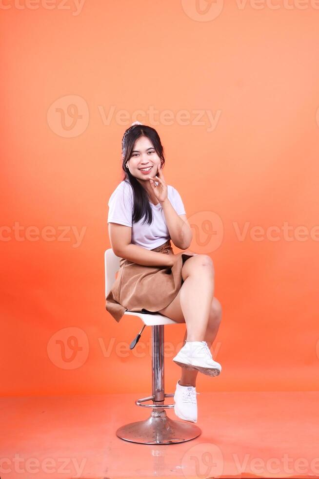 Young woman posing while sitting on a white chair isolated on an orange background photo